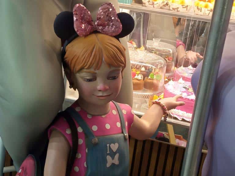 La escena presenta a una pareja de ancianos disfrutando de una merienda en un horno de Paiporta, una de las localidades de l'Horta Sud más afectadas por la DANA, mientras una niña juega con un carrito de juguete.